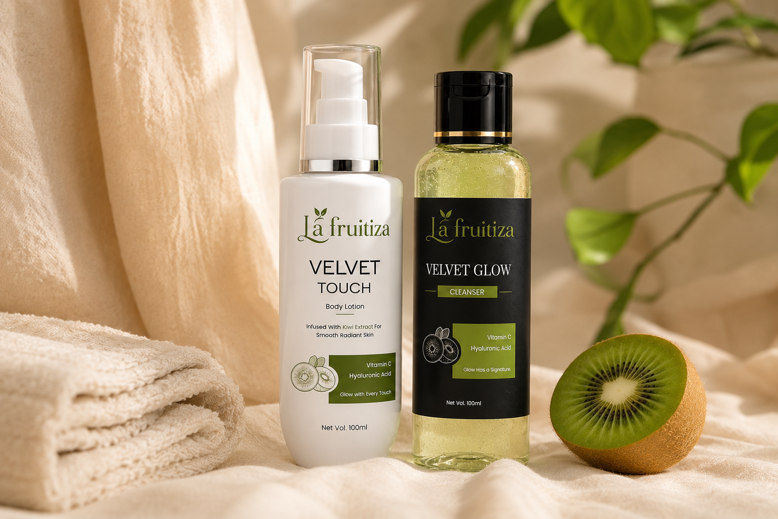 Two La fruitiza skincare bottles, Velvet Touch Body Lotion and Velvet Glow Cleanser, styled on a beige fabric surface with a folded towel, a kiwi slice, and green leaves in the background.